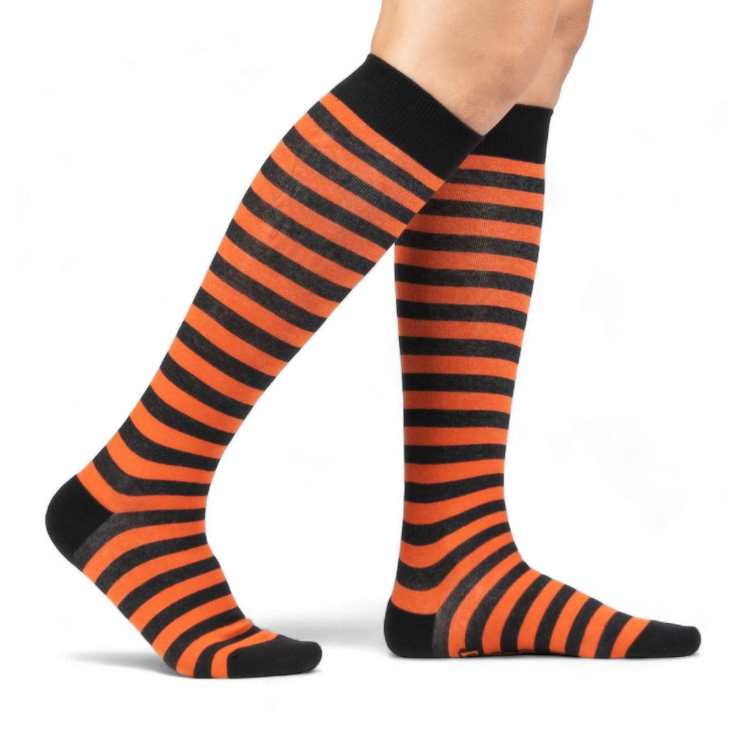Pumpkin orange and black striped knee high socks — model seated, side view