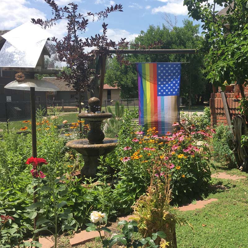 "For All" rainbow US flag displayed on garden pole outdoors