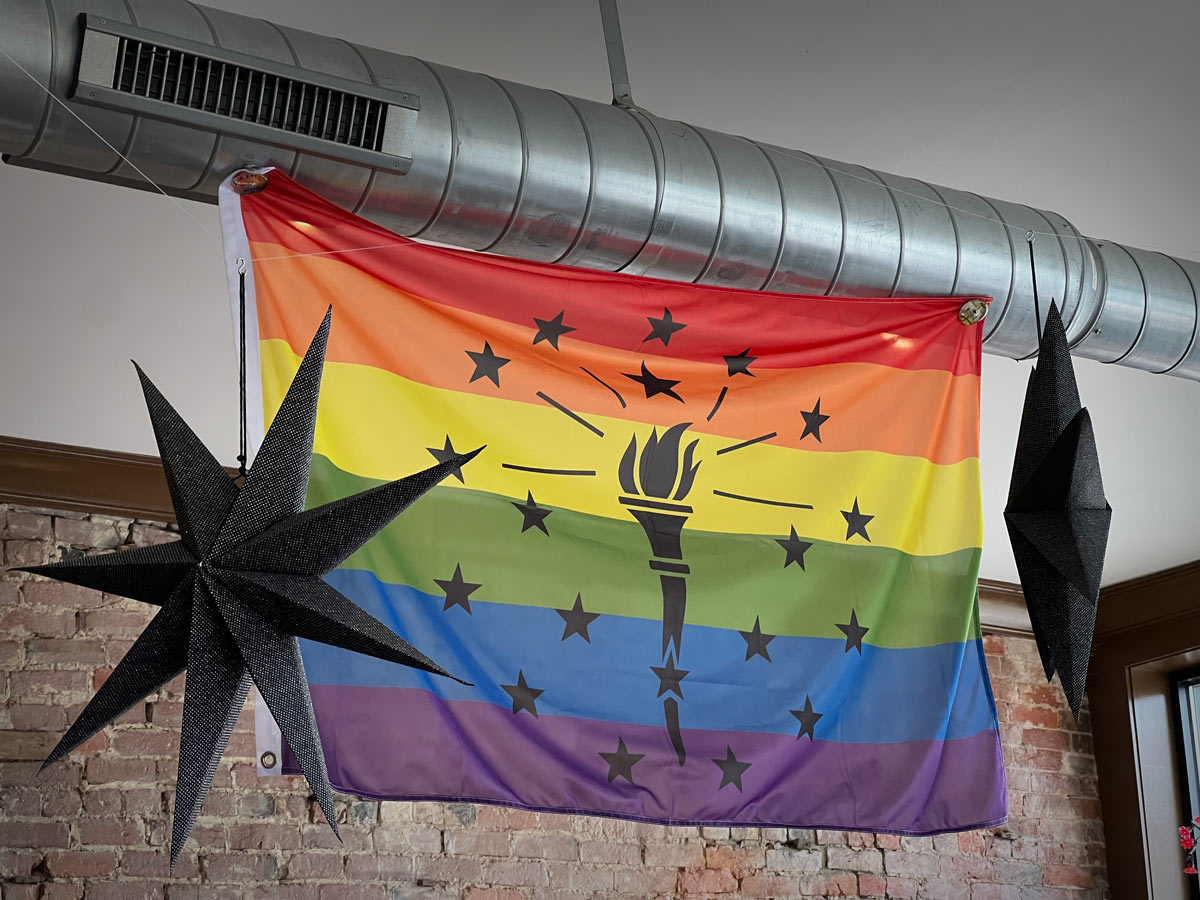 Indiana Rainbow Pride Flag hanging outdoors, rainbow stripes with black state design