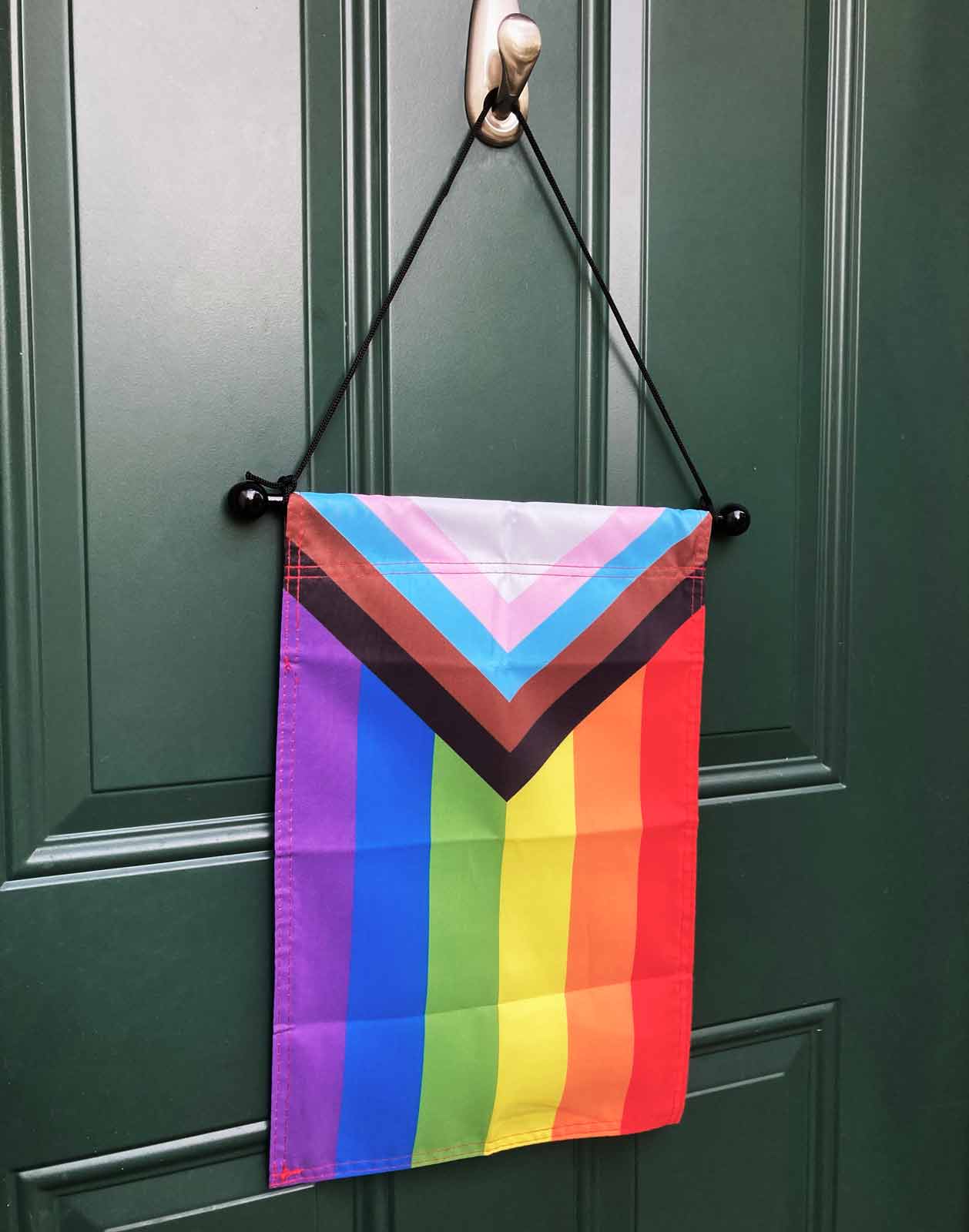 Natural wood wall rod with white cord — shown hanging Progress Pride garden flag on a door