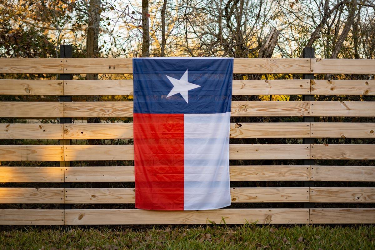 Texas flag displayed on a fence outdoors