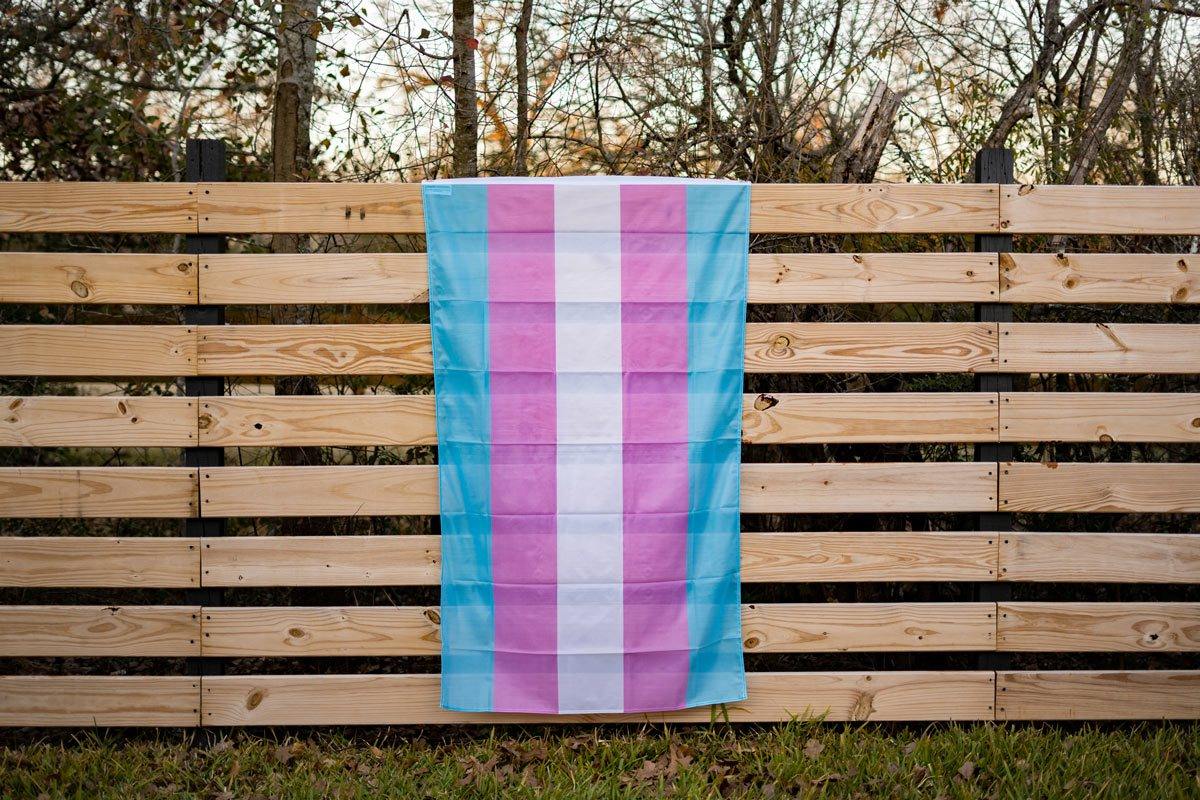 Transgender Pride flag displayed on a fence outdoors